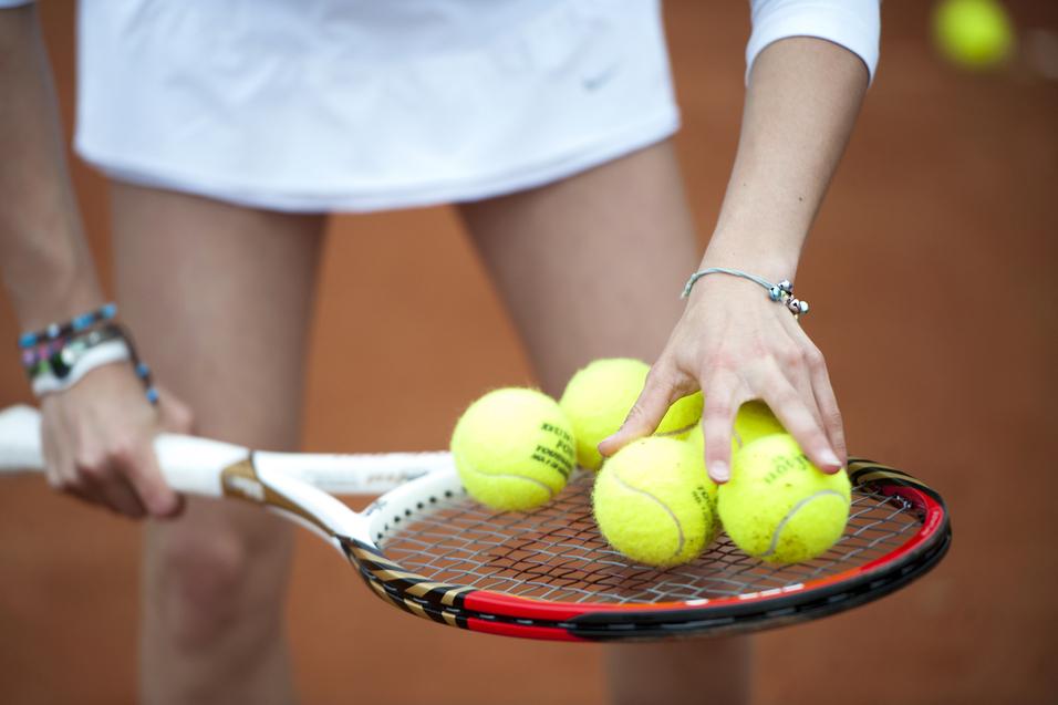 Hand greift mehrere gelbe Tennisbälle auf einem Tennisschläger, während die andere Hand die Schlägerhaltung stabilisiert.